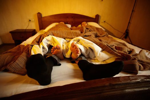 Newlyweds in clothes lying in bed. Groom in socks, barefoot bride