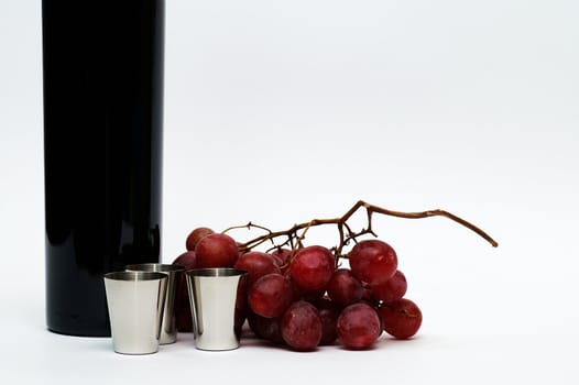 Three steel cups in front of red grape branch and a part of red vine bottle