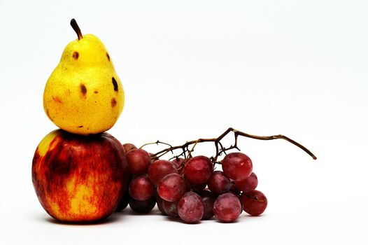 Yellow pear on top of red apple and red grape on white