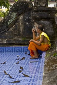 Young buddhist monk in a temple making a phone call
