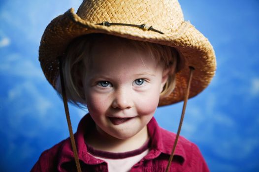 Little girl in front of blue wall wearing a cowboy hat with her tongue out