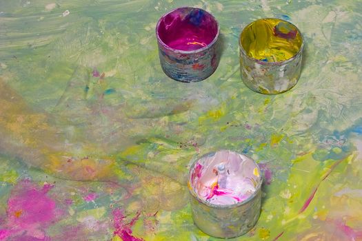 Cans with a paint for drawing by fingers and an illusive hand of the child on the painted spotty background