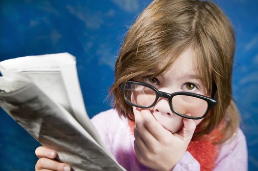 Shocked Young Girl Dressed Up in Reading Glasses Reading a Newspaper