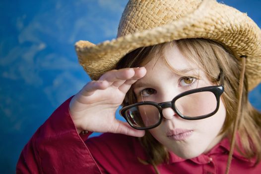 Little girl wearing a straw cowboy hat adjusts her glasses