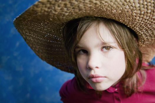 Little girl wearing a straw cowboy hat with a neutral expression