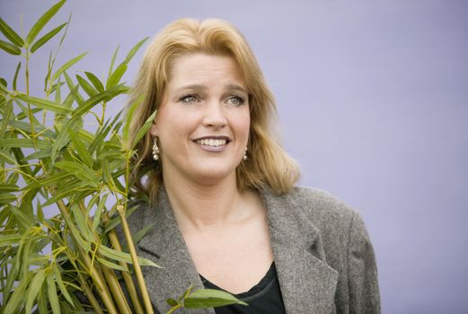 Woman in front of a purple wall carrying a leafy plant