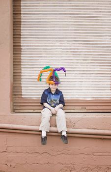 Young boy wearing a balloon hat sitting on a ledge