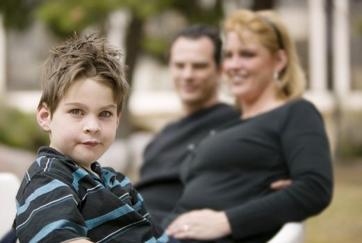 Little boy in the foreground smiles with his mom and dad in the background