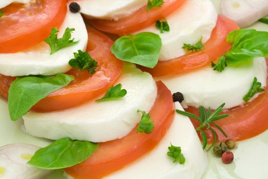 Caprese salad close-up with olive oil, green, black and pink pepper, shallot slices, parsley and rosemary