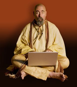 Funny guru sitting lotus style using a laptop computer