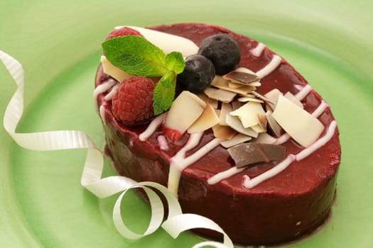 Raspberry mousse cake decorated with fruits and chocolate shavings on a green plate