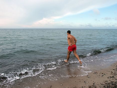 Happy young man running into the sea to swim on the beach