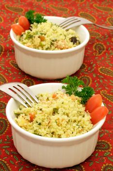 Two ramekins of coucous salad with forks on a colorful tablecloth