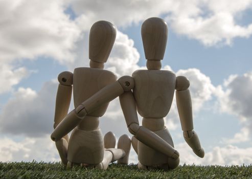 two wooden puppets as loving couple outside on green grass with blue sky