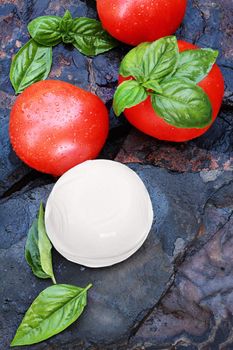 Ingredients for Caprese Salad. Fresh mozzarella cheese ball, basil, and tomatoes on a rustic slate background. 