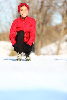 Winter runner getting ready running tying shoe laces. Beautiful young mixed race Asian / Caucasian female fitness model training outside. Copy space on snow.