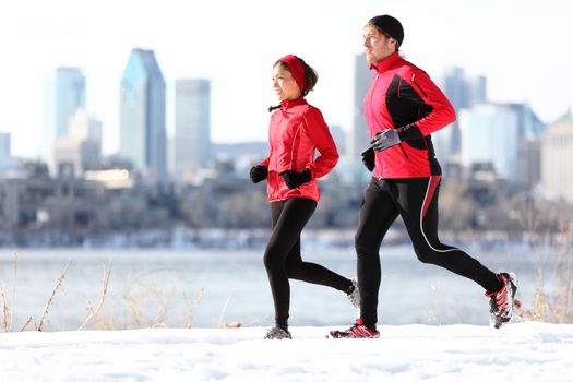 Runners running in winter snow with city skyline background. Healthy multiracial young couple. Asian woman runner and Caucasian man running with Montreal skyline, Quebec, Canada