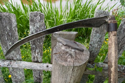scythe and whetstone supported on wooden fence