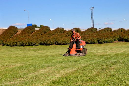 Mature man driving grass cutter in a sunny day