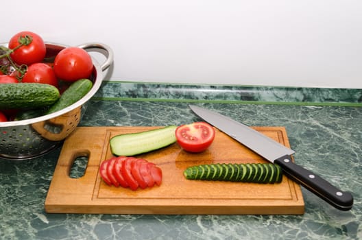 red tomato and green cucumbers slices with knife on board