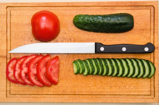 red tomato and green cucumbers slices with knife on board