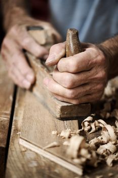 hands of a carpenter planing a plank of wood with a hand plane
