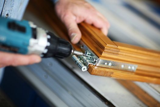 hands of a carpenter screwed a hinge on a wooden door