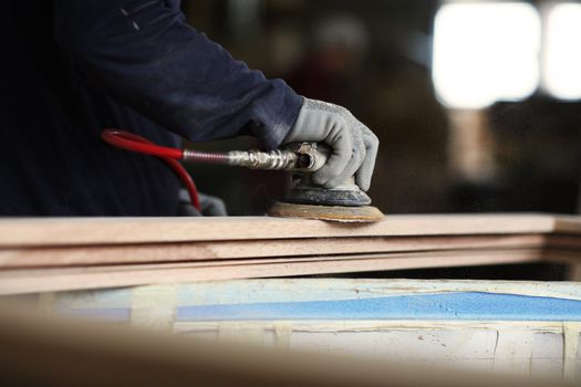 hands of a carpenter finish a wooden frame with a sander