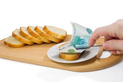 Hand spreads bread with thousand-roube banknote on small plate on chopping board