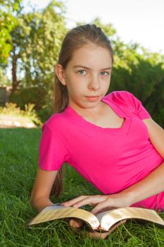 Teen girl reading the Bible outdoors lying on the grass