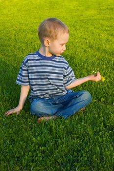 The four-year boy sits on a grass crossing legs