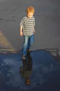 The four-year boy stands near to a pool and looks at the reflection in water