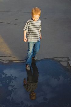 The four-year boy stands near to a pool and looks at the reflection in water