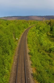The railway turns to the right between green wood hills