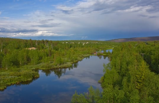 Clouds are reflected in silent northern small river among green hills