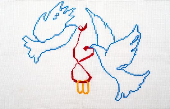 Embroidered good by cross-stitch pattern. White doves holding wedding rings