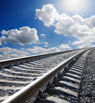 railway to horizon under cloudy sky with sun