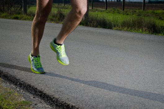 Running sport shoes outdoors in action on country road. Male shoes on young man training. Slight motion blur, focus on back running shoe.