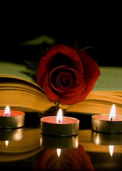 Open book and a red rose and candle on a black background