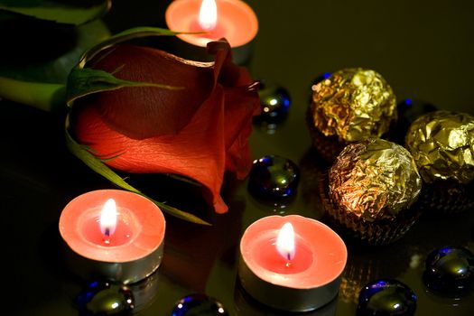 Red roses, candles burning in the night and candy wrapper