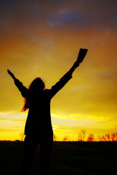 Woman staying with raised hands at the sunset time
