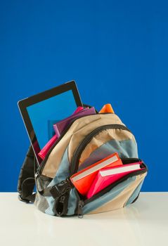 Backpack with colorful books and tablet PC on the blue background