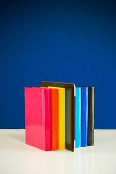 Row of colorful books and tablet PC over blue background