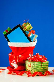 Tablet PC with heap of presents in red bag against blue background
