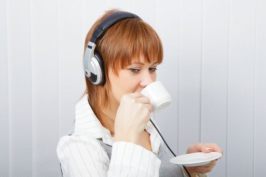 The girl in headphones with a microphone drinks coffee