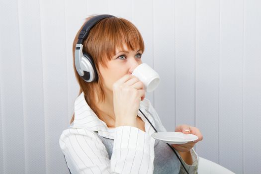 The girl in headphones with a microphone drinks coffee