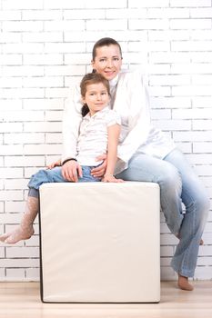 Mom and daughter in a similar dress sitting on a chair in the shape of a cube