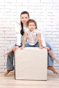Mom and daughter in jeans and white shirt sitting in a chair in the shape of a cube