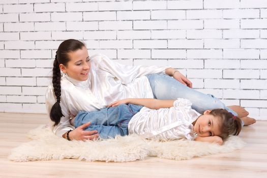 Mother and 5 year old daughter lying on a white fur rug beside the white stone wall