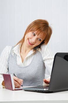 Attractive happy girl talking on the phone and writes simultaneously